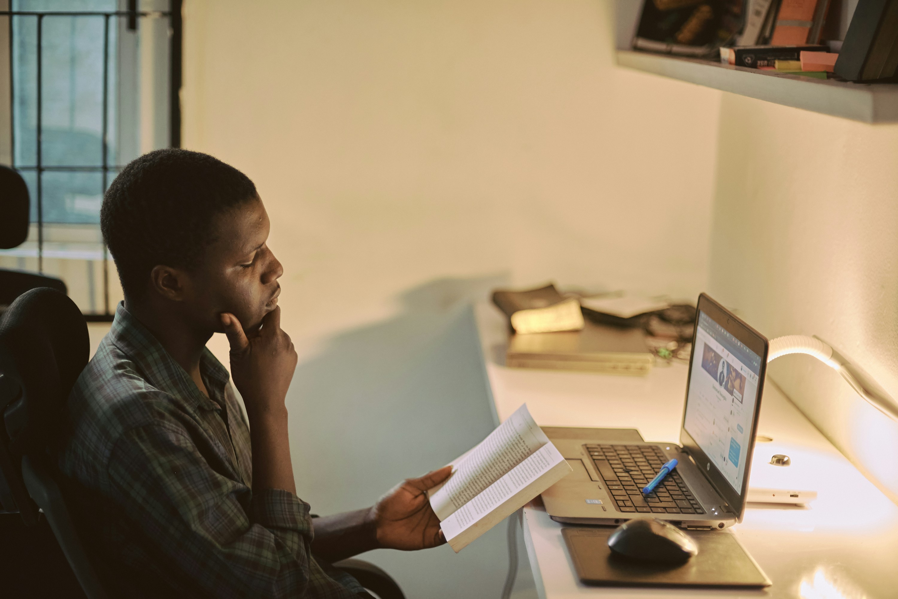 Portrait of a creative African man taking a break from work to read with his workspace blurred in the background